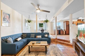 A living room with a sectional sofa, a coffee table, hanging plants, and a ceiling fan. - Welcome to Casa de Ladrillos - No House guests without prior approval from host. (Albuquerque)