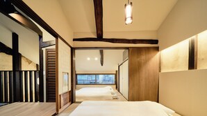 A hotel room with a wooden floor, a large bed, a window with a view, and a hanging light fixture. - Kyoto Machiya Kamogawa Gardens (Kyoto)