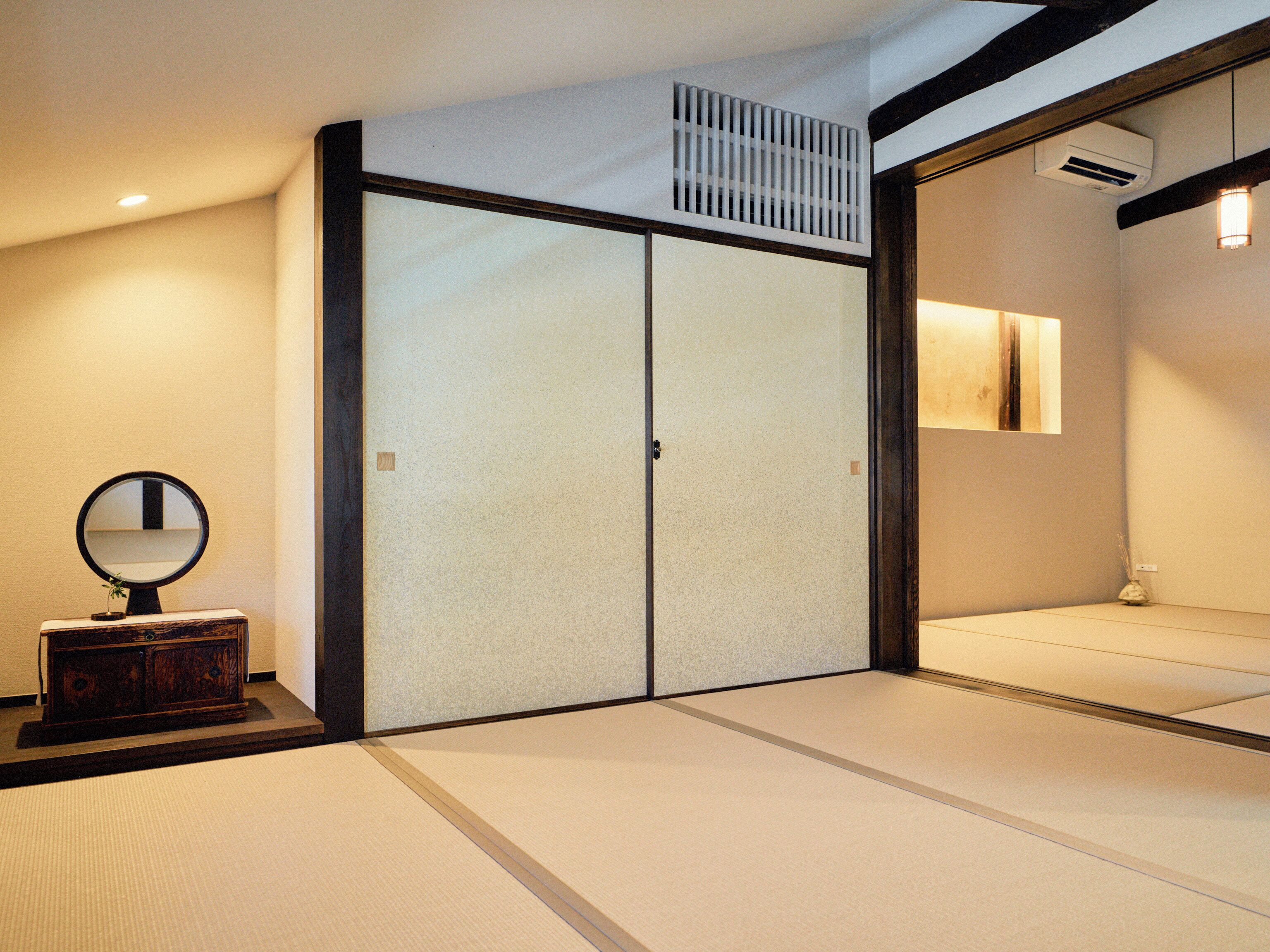 A traditional Japanese room with tatami flooring, a sliding shoji screen door, a small wooden cabinet with a mirror, and a wall-mounted air conditioning unit.