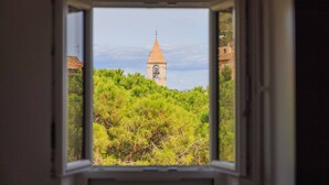 A window view of a church tower surrounded by greenery.