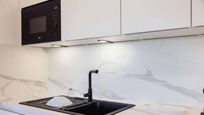 A kitchen with a black sink, a microwave, and a marble backsplash.