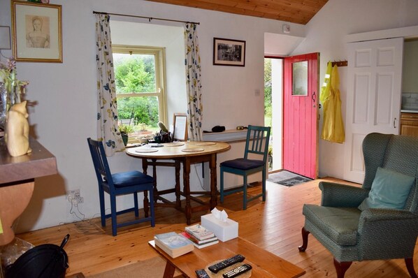 Una sala de estar acogedora con piso de madera, una mesa redonda para comer, dos sillas azules, un sillón verde y una pequeña estantería.