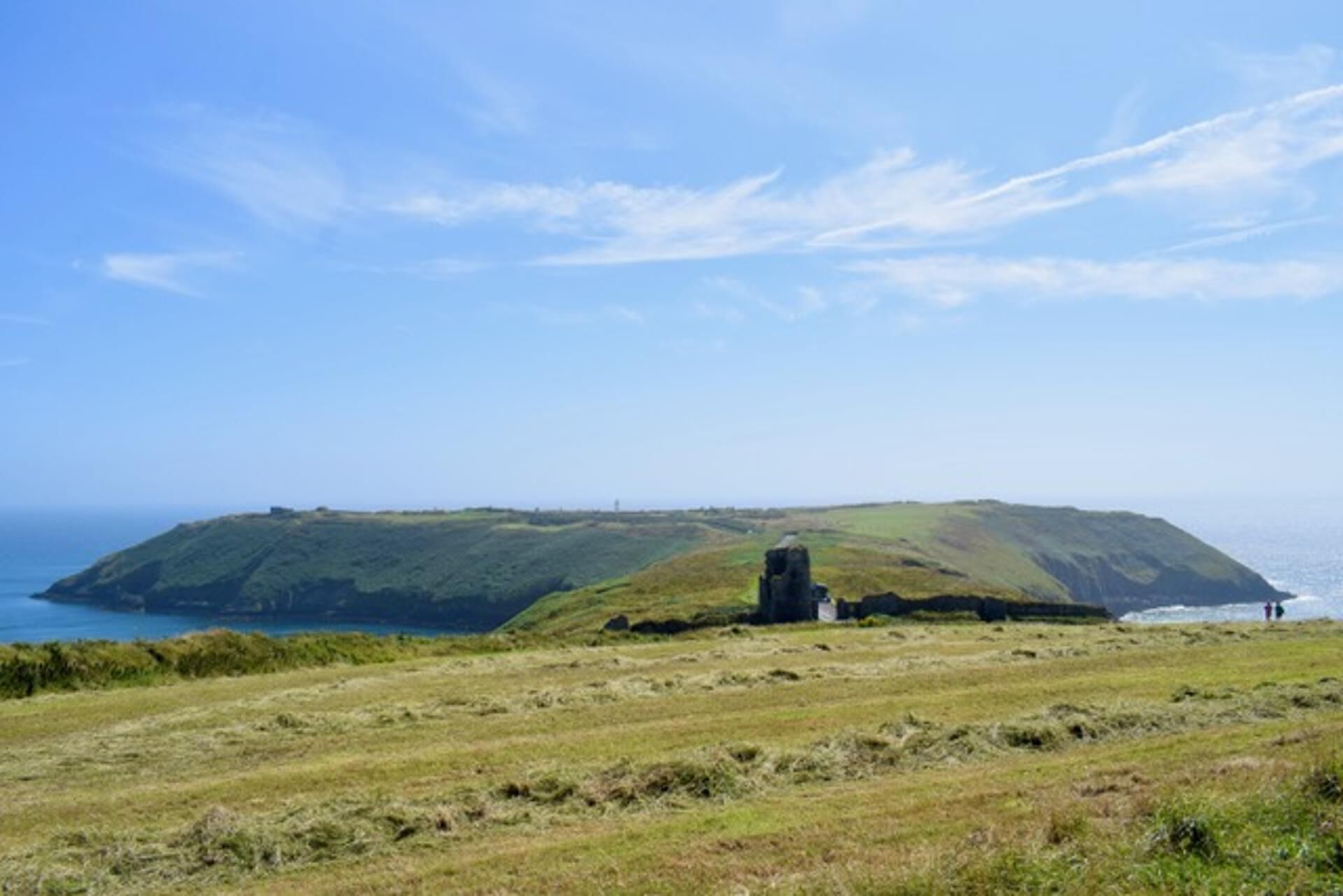 A coastal landscape with a grassy field, a small structure, and a view of the sea.
