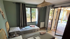 Une chambre avec deux lits, un fauteuil en osier, un ventilateur de plafond et une vue sur l’extérieur.