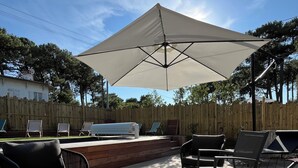 Une terrasse extérieure dotée d’un grand parasol, de mobilier d’extérieur et d’une plateforme en bois.