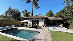 Un jardin avec une piscine, une terrasse en bois et un espace patio aménagé avec du mobilier d’extérieur.