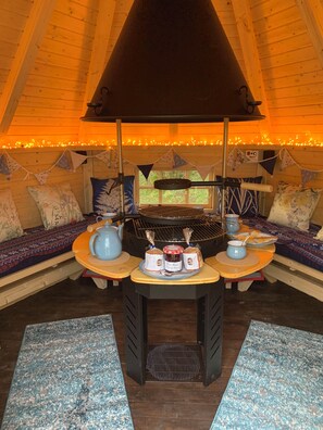 A cozy interior with a wooden ceiling, a central table with a grill, and seating with patterned cushions. - Cosy dog friendly cottage in an idyllic rural setting near amazing beaches (Boncath)