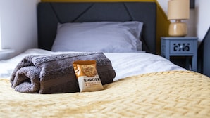 A neatly made bed with a folded towel and a packet of Border Oat Crumbles on the bed. - Entire Modern Home in Manchester For You (Manchester)
