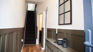 A hallway with a wooden floor, a staircase, a wall-mounted light fixture, and a door. - Entire Modern Home in Manchester For You (Manchester)