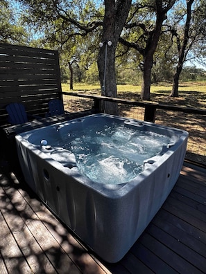 Een hottub op een houten terras, met een omheining en bomen op de achtergrond.