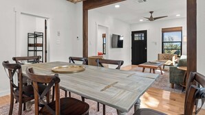 A spacious dining area with a wooden table and chairs, a ceiling fan, and a television in the background. - Starry Night Cottage 1 (Stonewall)