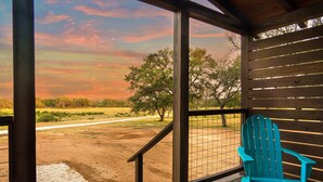 A wooden deck with a blue Adirondack chair, a view of a dirt path, and trees in the background. - Starry Night Cottage 1 (Stonewall)