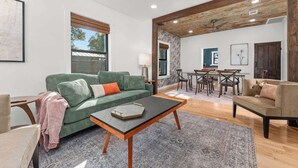 A living room with a green sofa, a coffee table, a dining area with a table and chairs, and a ceiling fan. - Starry Night Cottage 1 (Stonewall)
