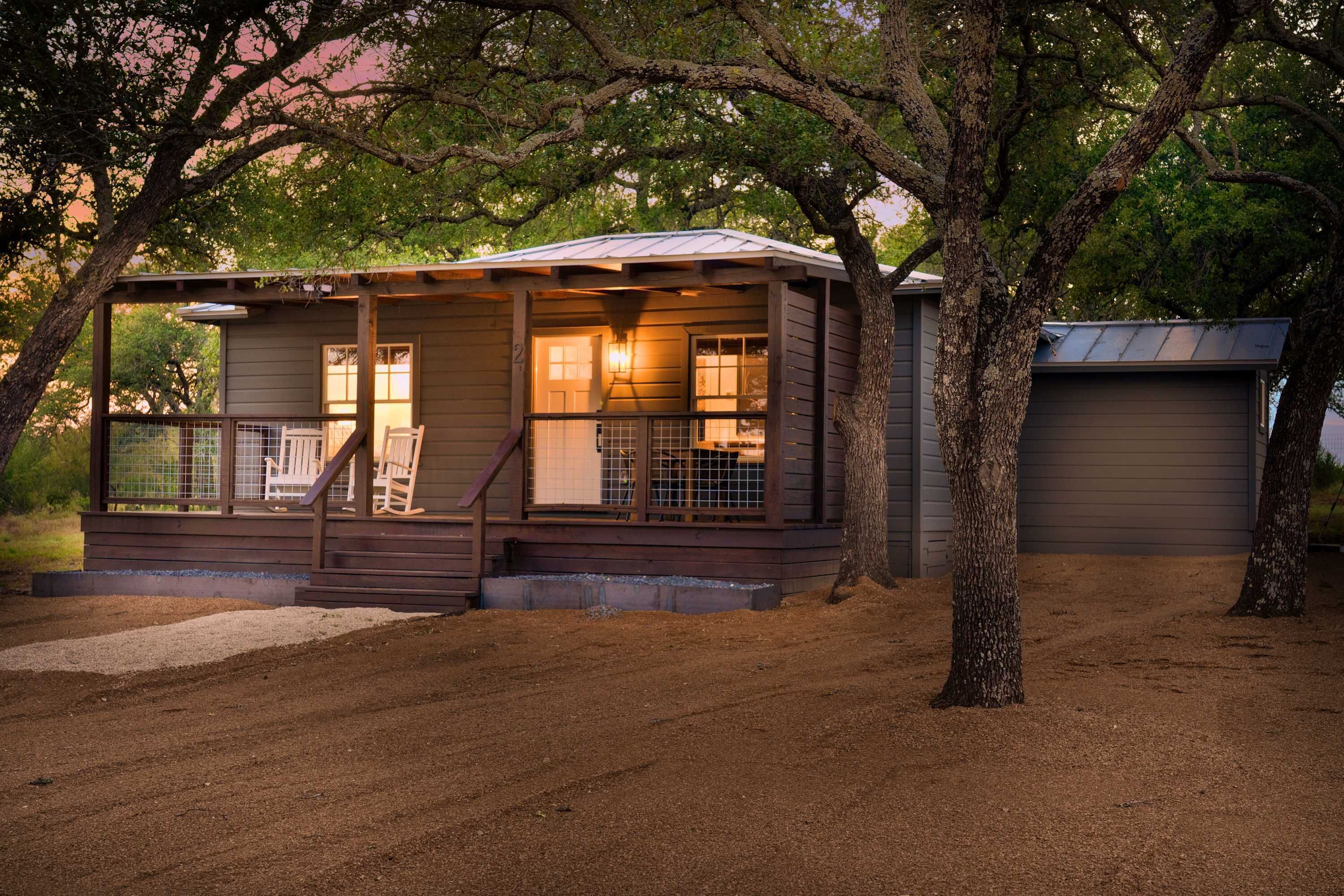 Uma cabana pequena e térrea com varanda, um deck cercado e uma garagem.
