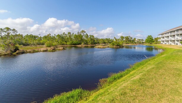 A serene lakeside view with a building featuring multiple balconies and a grassy area. - Romar Lakes 103B (Orange Beach)