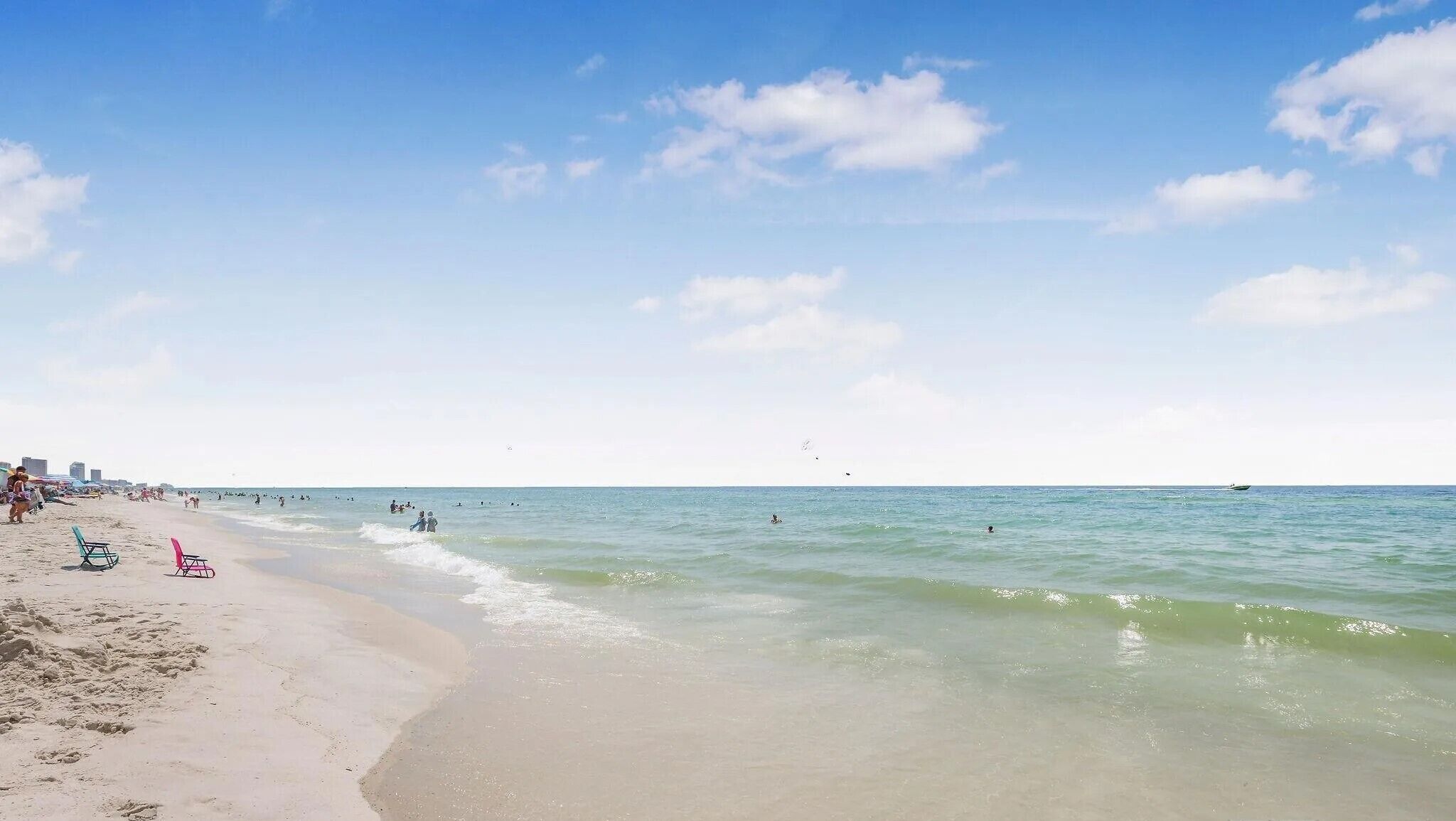 Una playa con cielos despejados, aguas tranquilas y algunas personas nadando.