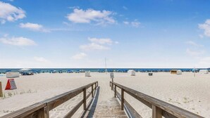 A wooden boardwalk leading to a sandy beach with umbrellas and beach huts. - Romar Lakes 103B (Orange Beach)