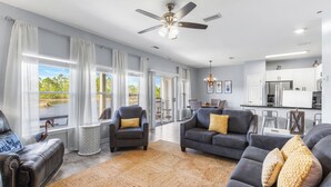 A spacious living room with a grey sofa, a dark armchair, and a large window with curtains. - Romar Lakes 103B (Orange Beach)