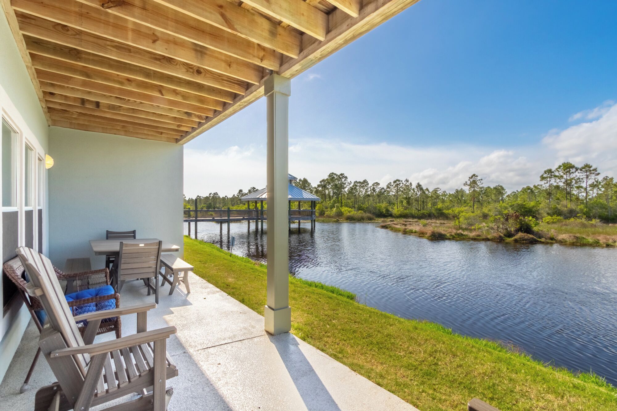 A covered patio with outdoor furniture, a view of a lake, and a wooden dock.