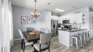 A modern kitchen with white cabinets, stainless steel appliances, and a central island with stools. - Romar Lakes 103B (Orange Beach)
