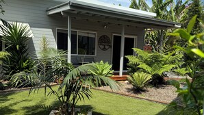 Una casa con césped cuidado, un porche y diversas plantas tropicales.