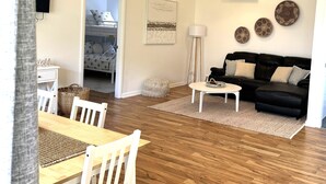 Una sala de estar con un sofá de cuero negro, una mesa de centro blanca y un comedor con una mesa de madera y sillas blancas.