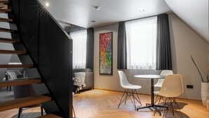 A modern loft with a wooden staircase, a dining area with white chairs, and a large abstract painting. - HOTEL NICE (Laupheim)