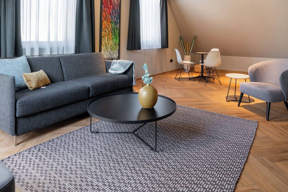 Una sala de estar moderna con un sofá gris, una mesa de centro negra, y un comedor con sillas blancas y una mesa pequeña.