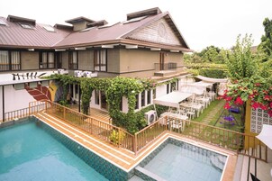 A hotel with a swimming pool, outdoor seating, and a garden area.