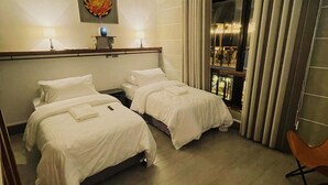 Ein Hotelzimmer mit zwei Betten, einem Fenster mit Vorhängen, einem Sessel und einem Gemälde an der Wand.