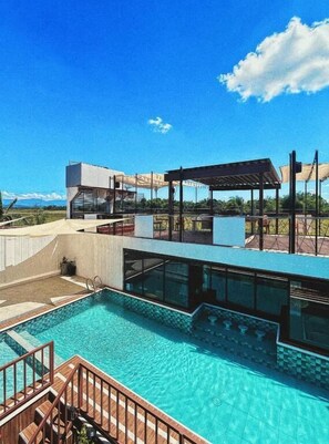 A modern pool area with a clear view of the pool, a covered seating area, and a building with large windows. - Urban Glamp Resort Iloilo (Oton)