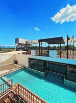 A modern pool area with a clear view of the pool, a covered seating area, and a building with large windows.