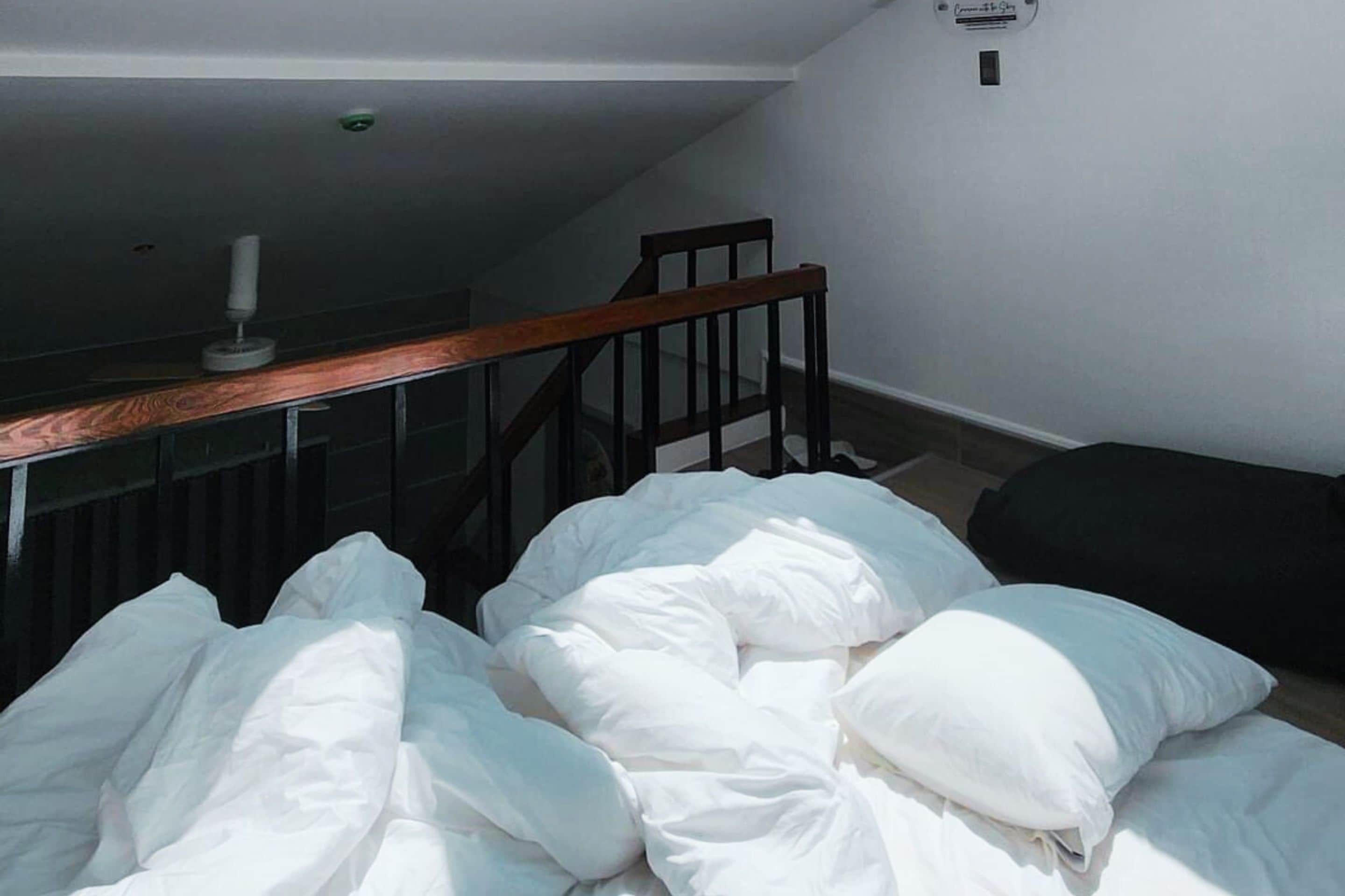 Een slaapkamer met een bed, kussens, een houten stoel en een trap.