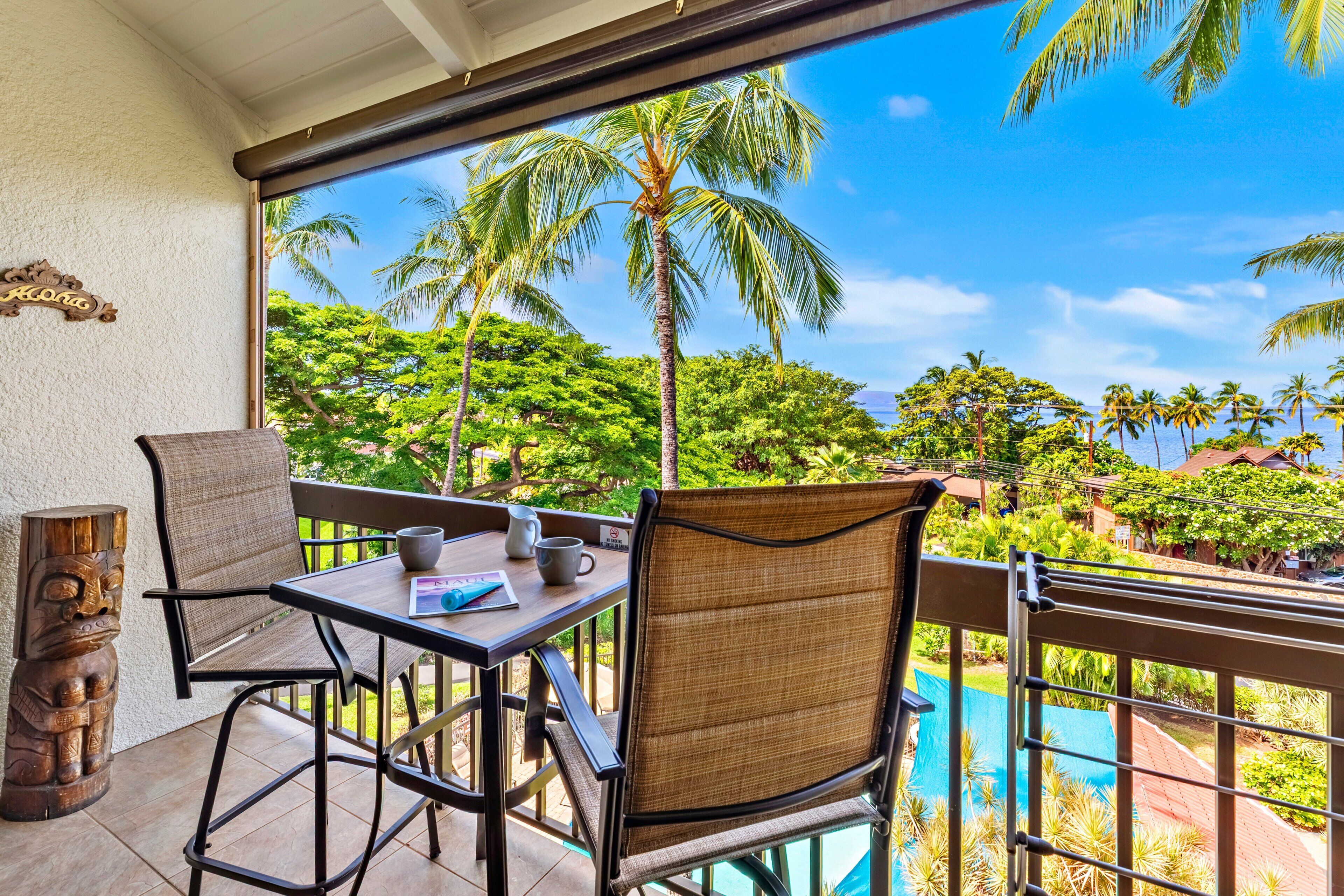 A balcony with a table and chairs, overlooking a pool and tropical vegetation.