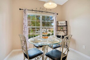 Zona pranzo con tavolo in vetro, quattro sedie, un lampadario, una finestra con tende e un cartello con la scritta 'Home'.
