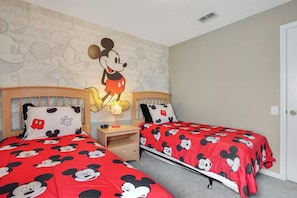 Une chambre avec deux lits, chacun agrémenté de linge de lit aux motifs de Mickey Mouse.