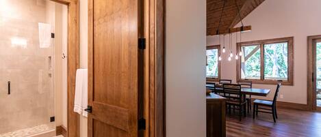 A wooden door leading to a bathroom with a glass shower and a dining area with a table and chairs.