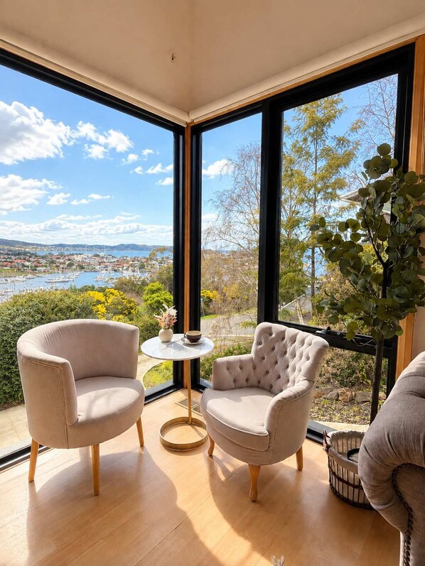 A room with two armchairs, a small round table, and a large window offering a view of a marina and landscape.