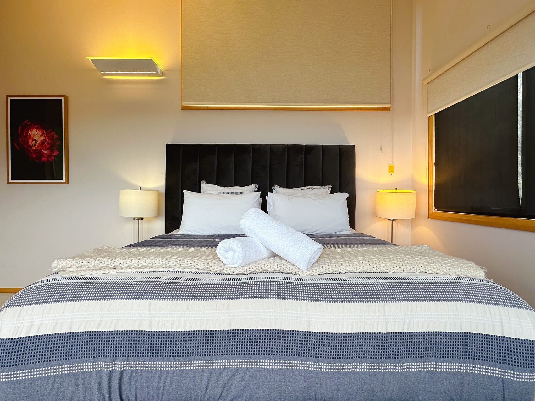 Quarto de hotel com uma cama grande, duas luminárias de cabeceira, uma obra de arte emoldurada na parede e uma janela com vista.