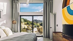 Ein Schlafzimmer mit einem großen Bett, einem Fernseher und Blick auf eine gebirgige Landschaft durch eine Glasschiebetür.