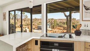 A modern kitchen with a large window overlooking a desert landscape, a built-in oven, and a countertop with a coffee machine.