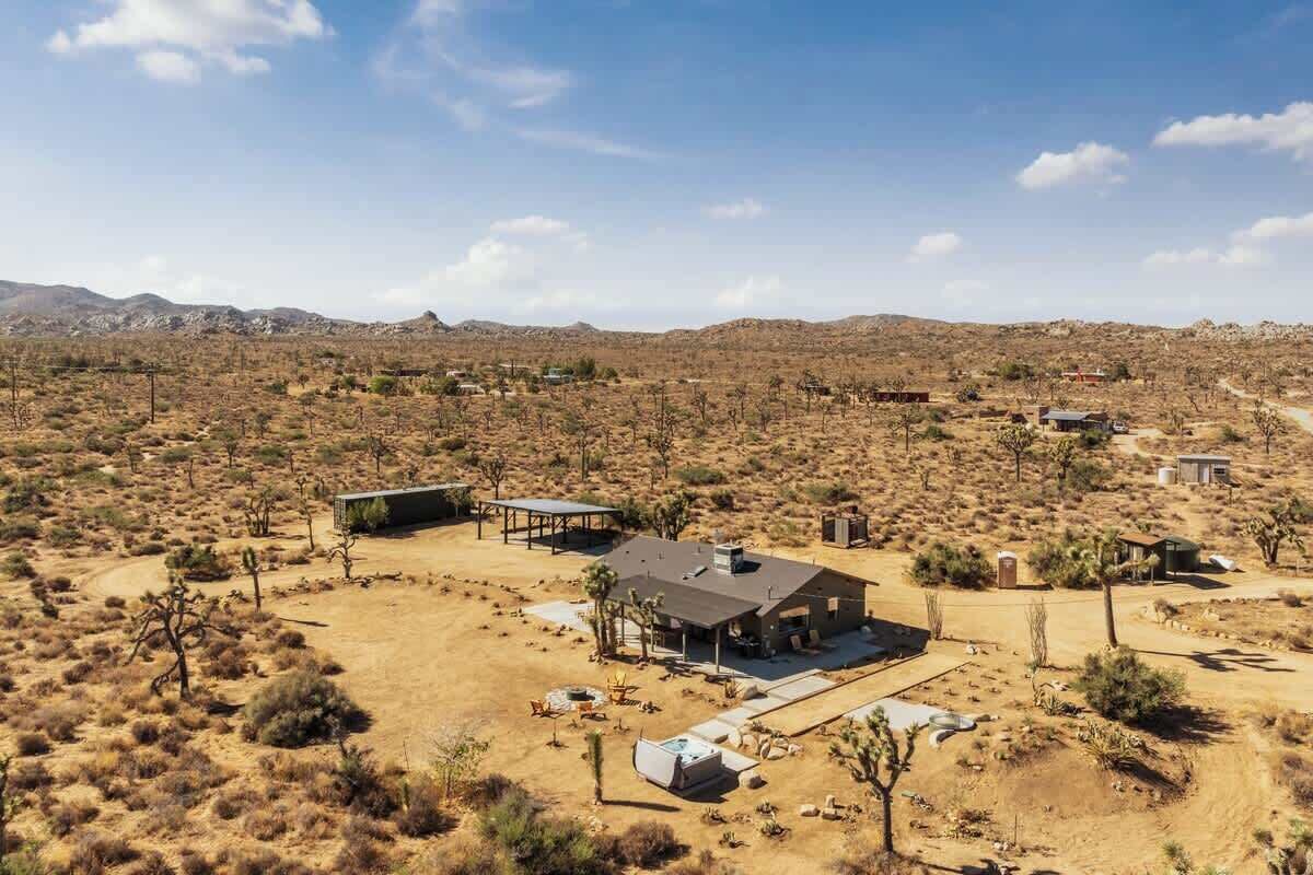 A desert landscape with a single house featuring a large patio, a covered outdoor area, and a view of distant mountains.