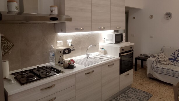 A modern kitchen with a gas stove, microwave, and built-in oven. There is a sink with a faucet, and a small countertop with a kettle and a water bottle. - Confortevole ed Ampio Appartamento in Alghero a Ridosso del Parco Tarragona (Alghero)