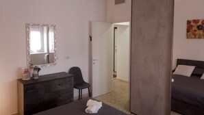 A bedroom with a bed, a dresser, a chair, a mirror, and a door leading to another room. - Confortevole ed Ampio Appartamento in Alghero a Ridosso del Parco Tarragona (Alghero)