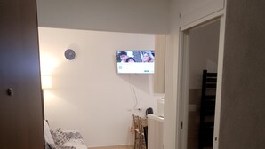 A room with a bed, a TV mounted on the wall, a small table, and a chair. - Confortevole ed Ampio Appartamento in Alghero a Ridosso del Parco Tarragona (Alghero)