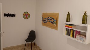 A room with a white wall, a dartboard, a wall-mounted art piece, a bookshelf with books, and a black chair. - Confortevole ed Ampio Appartamento in Alghero a Ridosso del Parco Tarragona (Alghero)