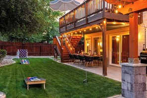Un patio trasero con terraza de madera, mesa de comedor para cuatro personas y una parrilla.