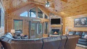 L’intérieur d’une cabane en rondins, avec un grand canapé en cuir, une cheminée en pierre et un téléviseur fixé au mur.