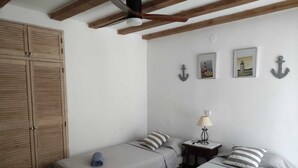 Habitació amb dos llits individuals, un armari de fusta, una taula petita amb una làmpada i quadres penjats a la paret.