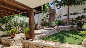 Un pati empedrat de pedra amb una pèrgola de fusta, plantes en testos i una paret de pedra.